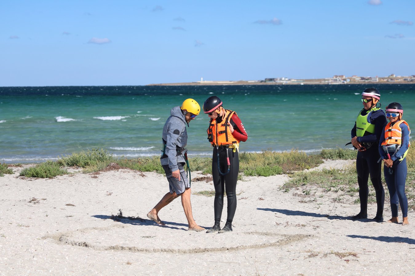 Quatre personnes sur une plage, casques et gilets, mer au fond.